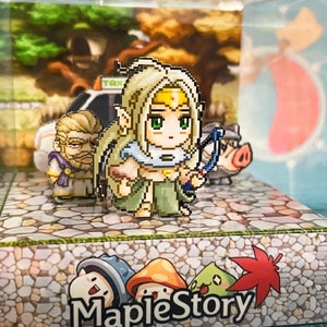 May include: A clear plastic cube display case with a miniature 3D scene of characters from the MapleStory video game. The scene includes a female character with blonde hair and a green dress, a male character with brown hair and a blue robe, and a pig. The base of the display case has a stone-like texture and the words "MapleStory" printed in black.