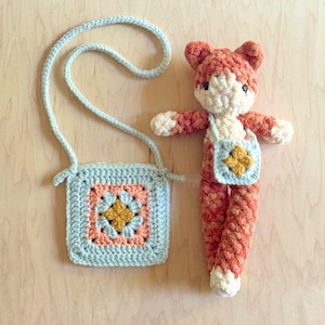 May include: A handmade crochet fox doll and matching light blue purse. The fox is orange and white, with a small purse featuring a flower design. The purse has a light blue strap. The doll is approximately 20 cm tall.