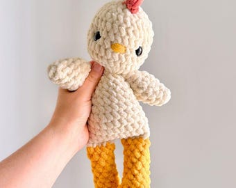 May include: A plush crochet chicken toy made from soft, cream-coloured yarn with a textured, bobble-like stitch pattern. It features a small pink comb on top, a yellow beak, two black plastic eyes, and bright yellow legs with defined feet.