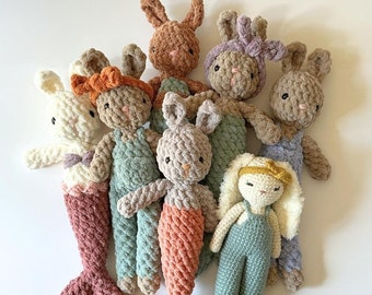 May include: A group of seven crocheted plush bunny toys in various colors, including brown, pink, white, and green. The bunnies are wearing overalls and have different colored bows on their heads.