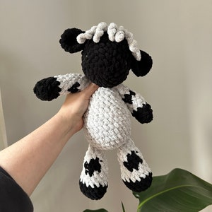 May include: A crocheted plush toy sheep with a black and white spotted pattern. The sheep has a black face and a white curly mane.