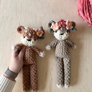 May include: Two crocheted deer plushies with floral headbands. The deer are brown and gray with white accents. The floral headbands are pink and yellow.
