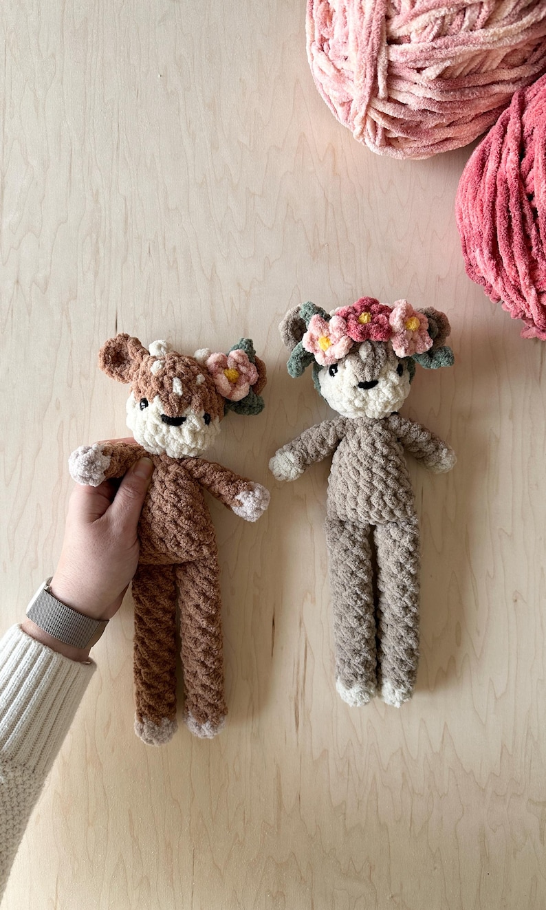 May include: Two crocheted deer plushies with floral headbands. The deer are brown and gray with white accents. The floral headbands are pink and yellow.