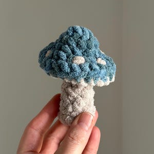 K&ouml;nnte beinhalten: Ein geh&auml;keltes Pilzspielzeug mit einem blauen und wei&szlig;en Hut und einem beigefarbenen Stiel.