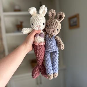 May include: Two crocheted stuffed bunny toys. One is white with a pink mermaid tail and the other is brown with blue dungarees.