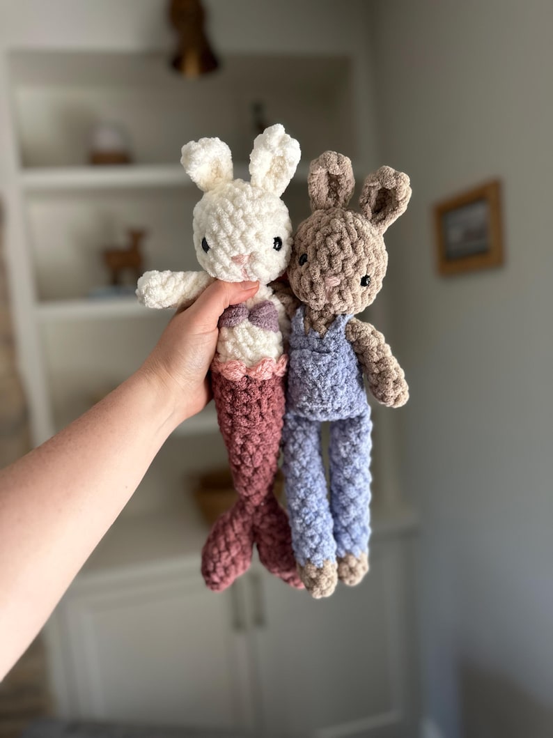 May include: Two crocheted stuffed bunny toys. One is white with a pink mermaid tail and the other is brown with blue dungarees.