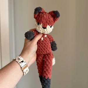May include: A crocheted fox plush toy with a red body, white face, and black ears and feet.