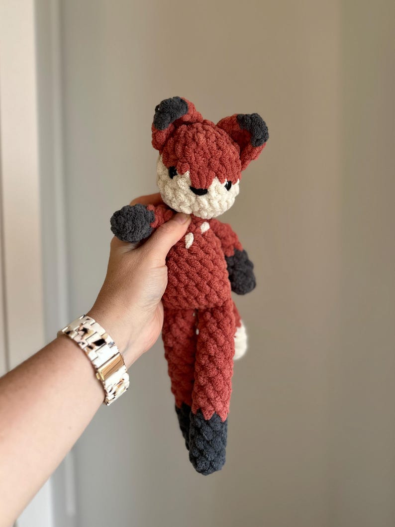 May include: A crocheted fox plush toy with a red body, white face, and black ears and feet.