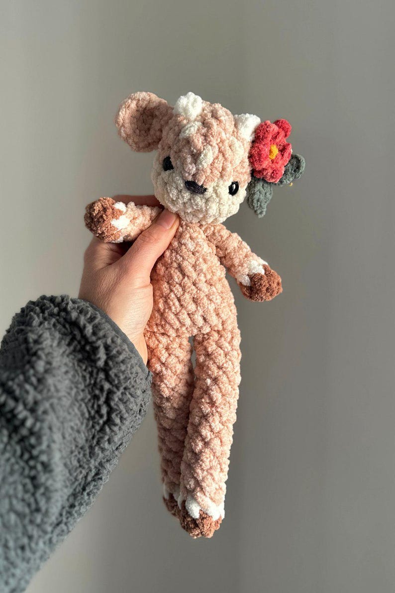 K&ouml;nnte beinhalten: Ein geh&auml;keltes rosa Hirsch-Pl&uuml;schtier mit wei&szlig;en Akzenten und einer roten Blume auf dem Kopf.