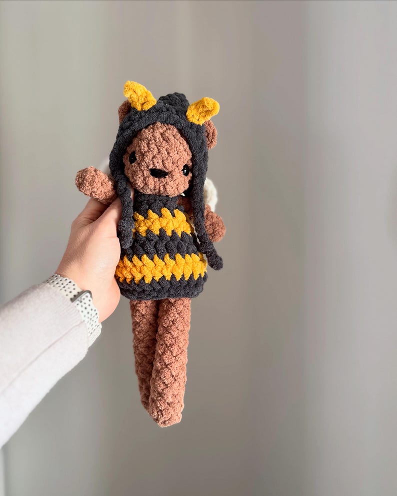 May include: A crocheted brown teddy bear wearing a black and yellow bee costume with a pointed hood and antennae.
