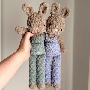May include: Two crocheted bunny plush toys with brown fur and overalls. One bunny is wearing green overalls and the other is wearing blue overalls.