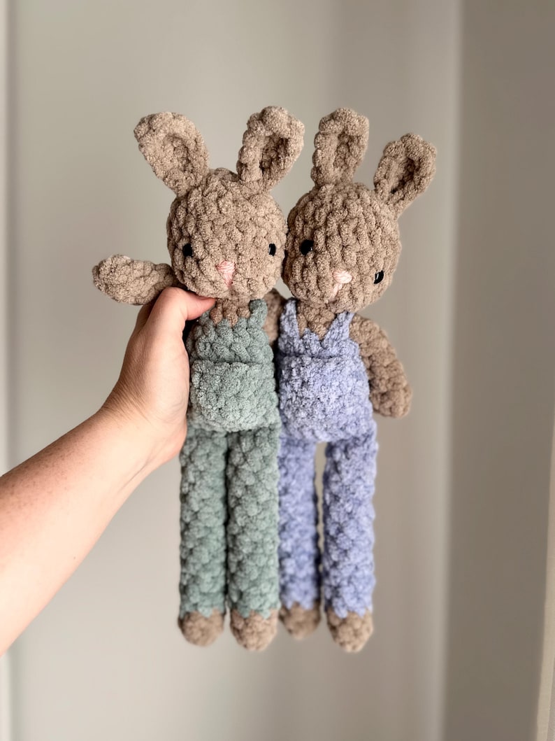 May include: Two crocheted bunny plush toys with brown fur and overalls. One bunny is wearing green overalls and the other is wearing blue overalls.