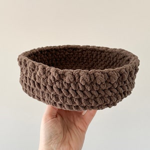 May include: A brown crocheted basket with a round shape. The basket is made with a thick yarn and has a textured surface.