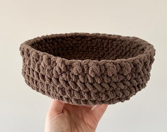 May include: A brown crocheted basket with a round shape. The basket is made with a thick yarn and has a textured surface.