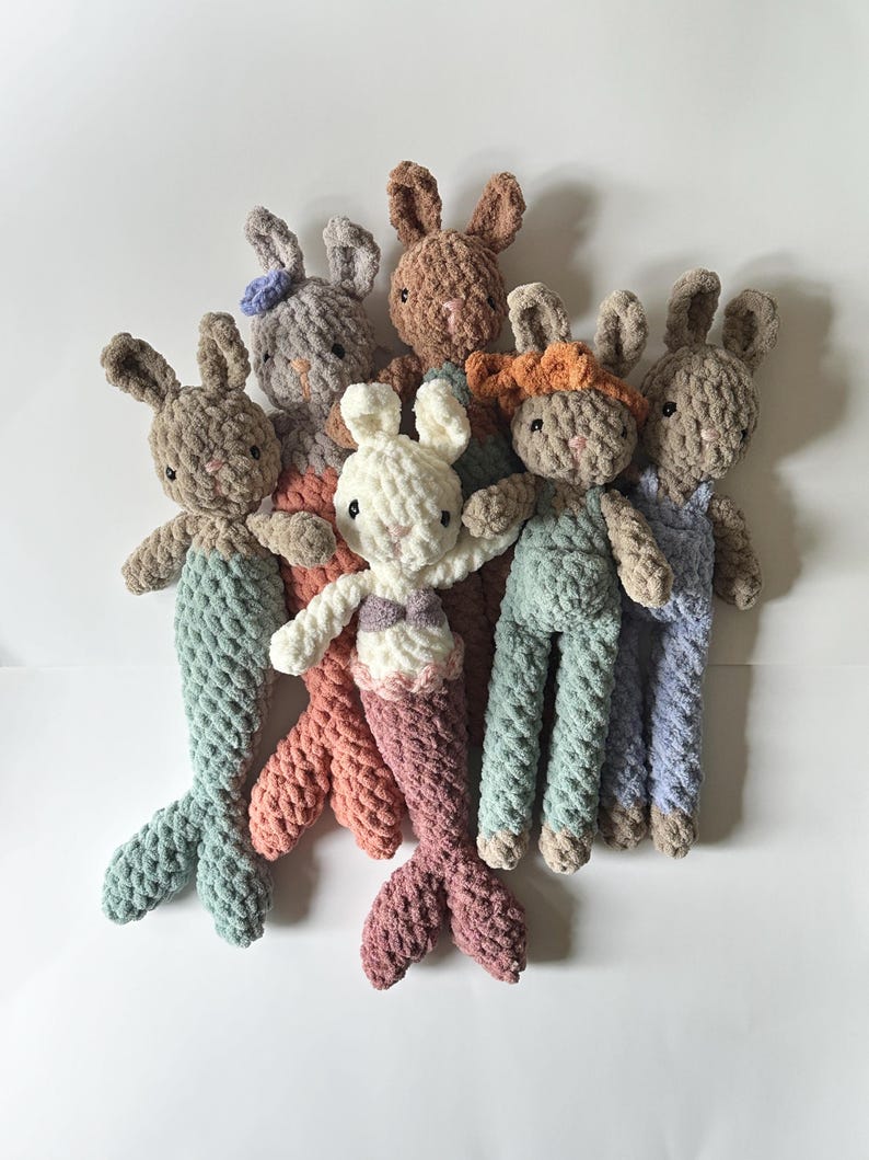 May include: A group of six crocheted plush bunny toys. The bunnies are in various colours, including brown, grey, white, orange, and blue. Some of the bunnies have mermaid tails.