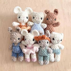 Puede incluir: Una colección de siete pequeñas figuras de animales tejidas a ganchillo con hilo suave y texturizado. Las figuras tienen orejas redondas, ojos de botón negros, narices bordadas y visten conjuntos en colores como naranja, azul, rosa y verde.