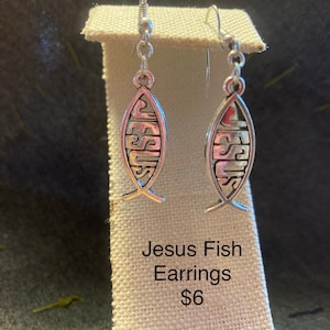 May include: Silver Jesus fish earrings with a simple design. The earrings are on a white fabric background. Jesus Fish Earrings $6. Sterling silver ear wires $2 extra.