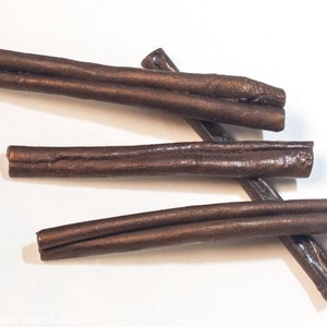 May include: Four brown leather cords, each about 10 inches long, are arranged in a random pattern on a white surface.