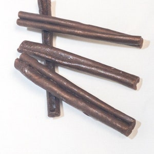 May include: Four brown leather dog chews in the shape of long sticks. The chews are arranged in a criss-cross pattern on a white surface.
