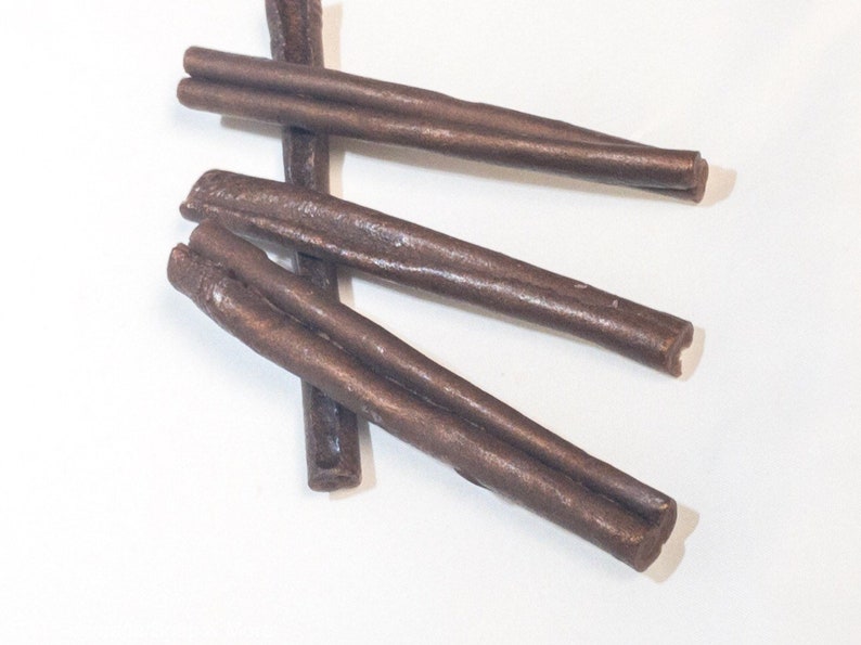 May include: Four brown leather dog chews in the shape of long sticks. The chews are arranged in a criss-cross pattern on a white surface.