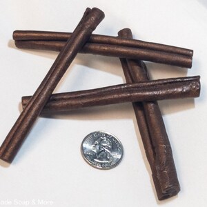 May include: Four brown cinnamon sticks arranged in a cross pattern on a white surface. A US quarter is placed in the center for size comparison.