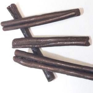 May include: Three brown licorice sticks, each about 10 inches long, are arranged in a criss-cross pattern on a white background.