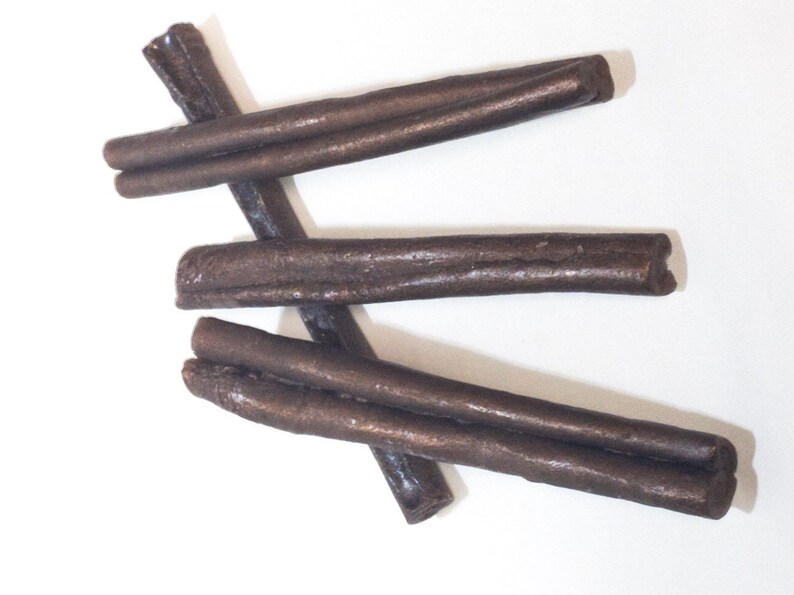 May include: Three brown licorice sticks, each about 10 inches long, are arranged in a criss-cross pattern on a white background.
