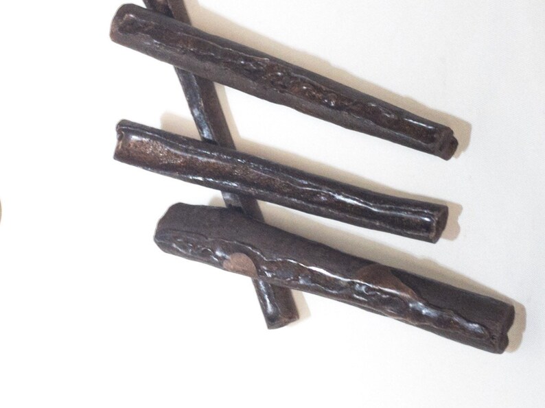 May include: Four dark brown sticks with a rough, textured surface. The sticks are arranged in a criss-cross pattern.