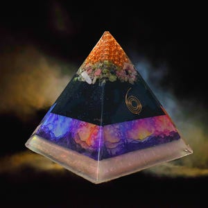 May include: A layered pyramid with a clear base, a dark blue central section with a gold spiral, and a top layer of orange and pink crystals. The pyramid has a colourful, artistic design with a galaxy-like appearance.