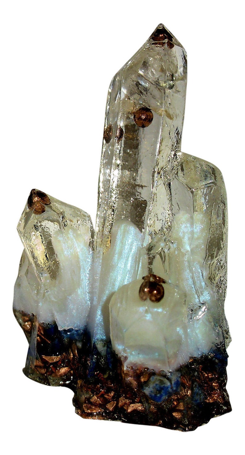 May include: A cluster of clear quartz crystals with copper-colored inclusions and accents. The crystals have a pearly white base with dark blue and copper-colored elements at the bottom. The crystals are arranged in a vertical formation.