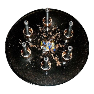 May include: A black circular tray with seven metal posts, each with a copper ring. A small, colourful, square-shaped object is in the centre of the tray.