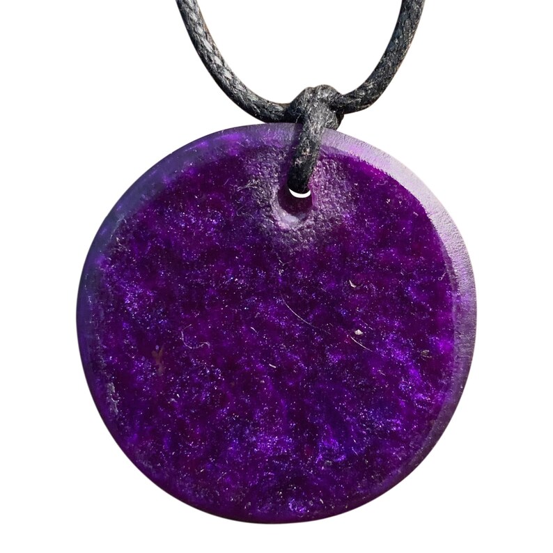 May include: A round, purple pendant with a black cord. The pendant has a speckled, glittery texture.