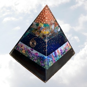 May include: A handcrafted pyramid with a copper top and a base adorned with a floral design. The pyramid features a dark blue interior with embedded colorful stones and a copper coil. The pyramid is a unique decorative item.