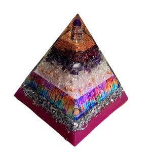May include: A multi-layered pyramid sculpture with a magenta base. The pyramid features layers of clear crystals, amethyst, copper wire, and a colorful forest scene. The top is capped with a purple crystal.