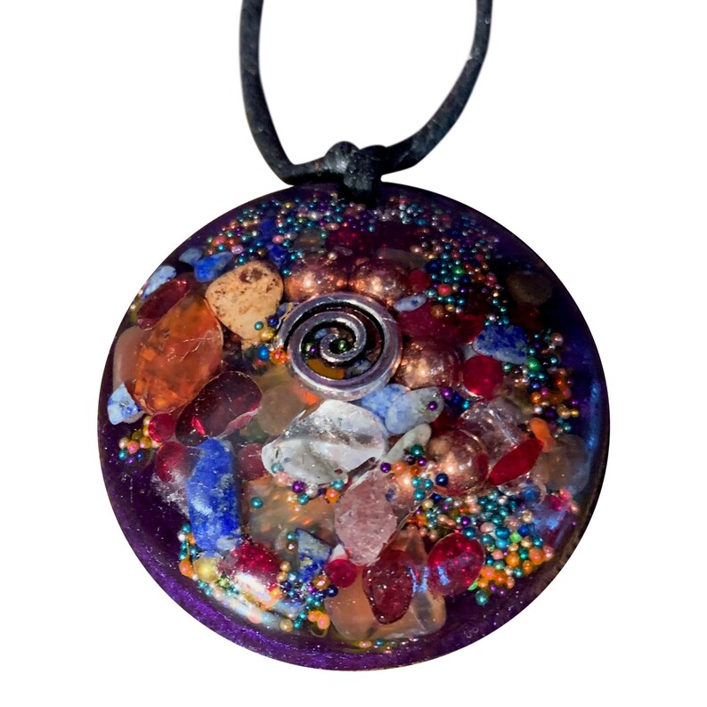 May include: A round, purple, resin pendant with a silver spiral charm. The pendant is filled with various colourful crystals and beads, including red, blue, orange, and white.