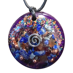 May include: A round, purple, resin pendant with a silver spiral charm. The pendant is filled with various crystals, including blue lapis lazuli, copper, and clear quartz.