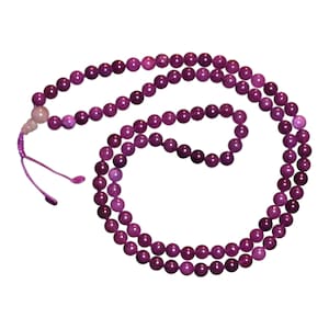 May include: A purple gemstone mala with a pink bead at the top. The mala is made of round beads and is strung on a cord.