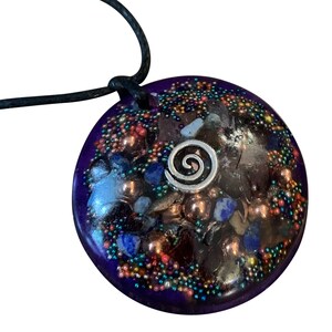 May include: A purple pendant with a silver spiral design and embedded crystals and beads. The pendant is on a black cord.