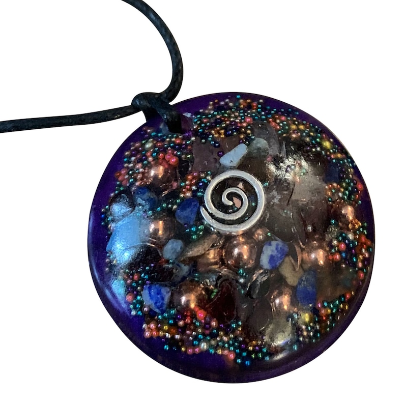 May include: A purple pendant with a silver spiral design and embedded crystals and beads. The pendant is on a black cord.