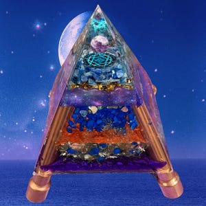 Könnte beinhalten: Eine mehrschichtige Pyramiden-Skulptur mit transparentem Äußeren. Sie zeigt blaue, violette, orange und goldene Elemente vor einem himmlischen Hintergrund. Kupferstäbe bilden die Struktur, und die Basis hat kupferfarbene Füße. Die Pyramide ist etwa 15 cm hoch.