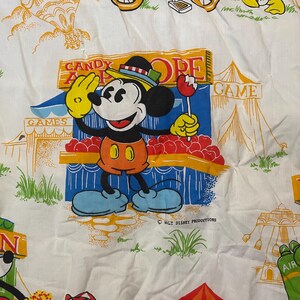 Puede incluir: Una tela blanca con una colorida ilustraci&oacute;n de Mickey Mouse en un carnaval. Mickey sostiene una manzana de caramelo y saluda. Las palabras "CANDY APPLE STORE" y "GAMES" son visibles. La imagen es un dise&ntilde;o de Walt Disney Productions.