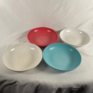 May include: Four colorful bowls in red, white, cream, and turquoise. The bowls are round with a speckled texture. The bowls are likely for serving food.