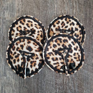 May include: Four leopard print fabric nursing pads with black trim and black buttons.