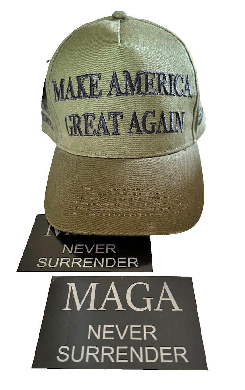 May include: A green baseball cap with the text "MAKE AMERICA GREAT AGAIN" embroidered in black. The cap is sitting on top of two black stickers with the text "Maga Never Surrender" in white.