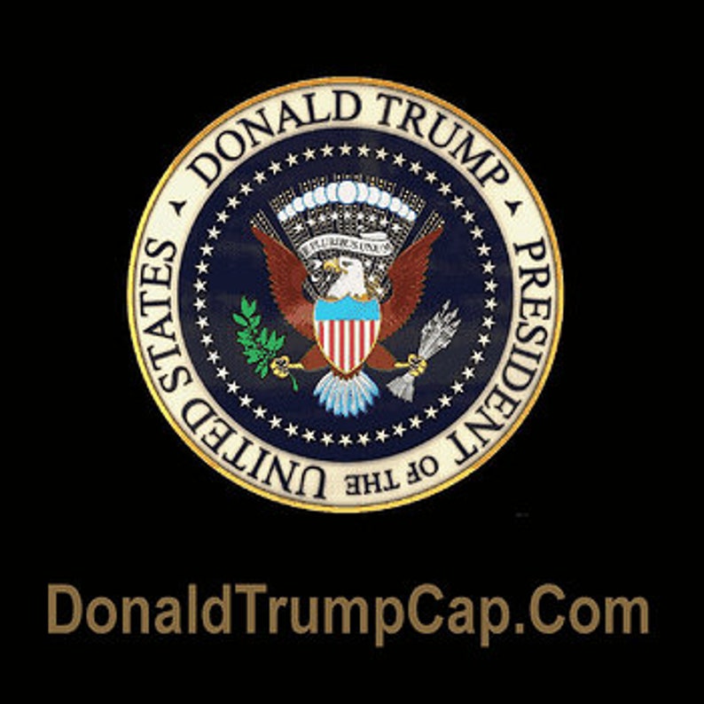 May include: A blue and gold presidential seal with the words "Donald Trump President of the United States" around the edge. The seal features a bald eagle with a shield on its chest and a banner that reads "E Pluribus Unum". The text "DonaldTrumpCap.com" is displayed below the seal.