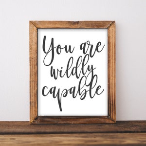 May include: A framed print with the text "You are wildly capable" in black cursive font on a white background. The frame is made of wood and has a brown finish.