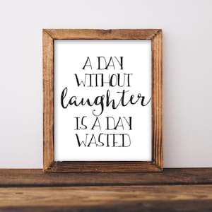 Puede incluir: Una impresi&oacute;n enmarcada con fondo blanco y texto negro que dice "A day without laughter is a day wasted". El marco es de madera marr&oacute;n.