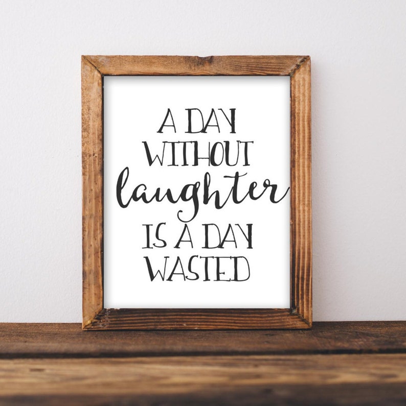 Puede incluir: Una impresi&oacute;n enmarcada con fondo blanco y texto negro que dice "A day without laughter is a day wasted". El marco es de madera marr&oacute;n.