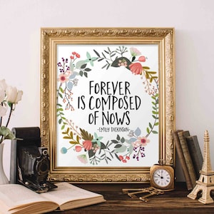 Puede incluir: Una impresión enmarcada en dorado con fondo blanco y una corona de flores que rodea la cita "Forever is composed of nows - Emily Dickinson".