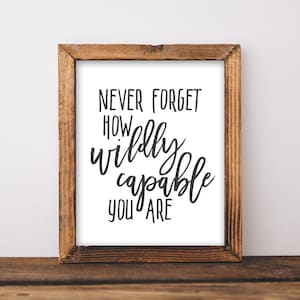 May include: A framed print with a white background and black text that reads "Never forget how wildly capable you are". The frame is made of wood and has a brown finish.